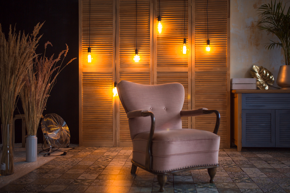 Rustikaler Sessel in dunklem Raum mit Hintergrundbeleuchtung durch einzelne hängende Glühbirnen